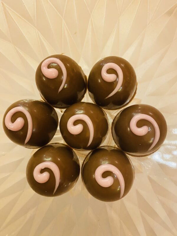 A close up of seven chocolate balls with pink swirls